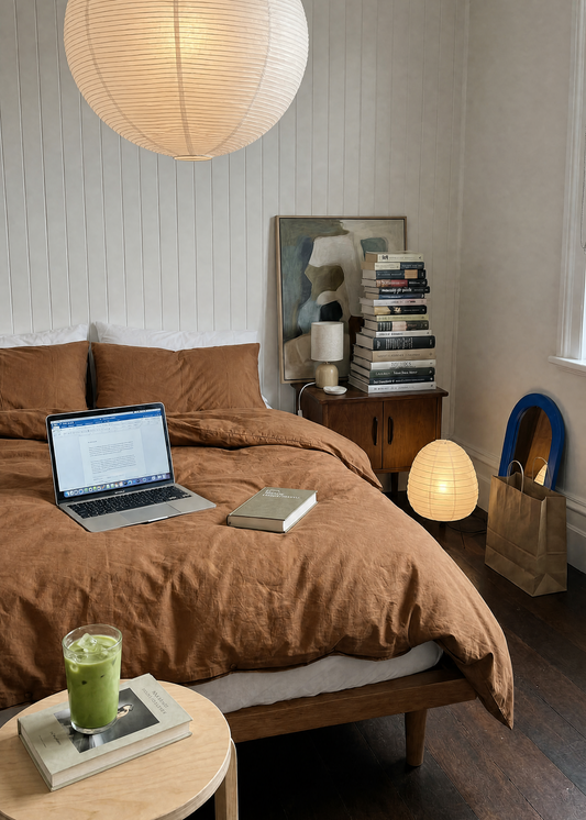Modern bedroom with brown bedding, laptop, and books on a wooden nightstand.