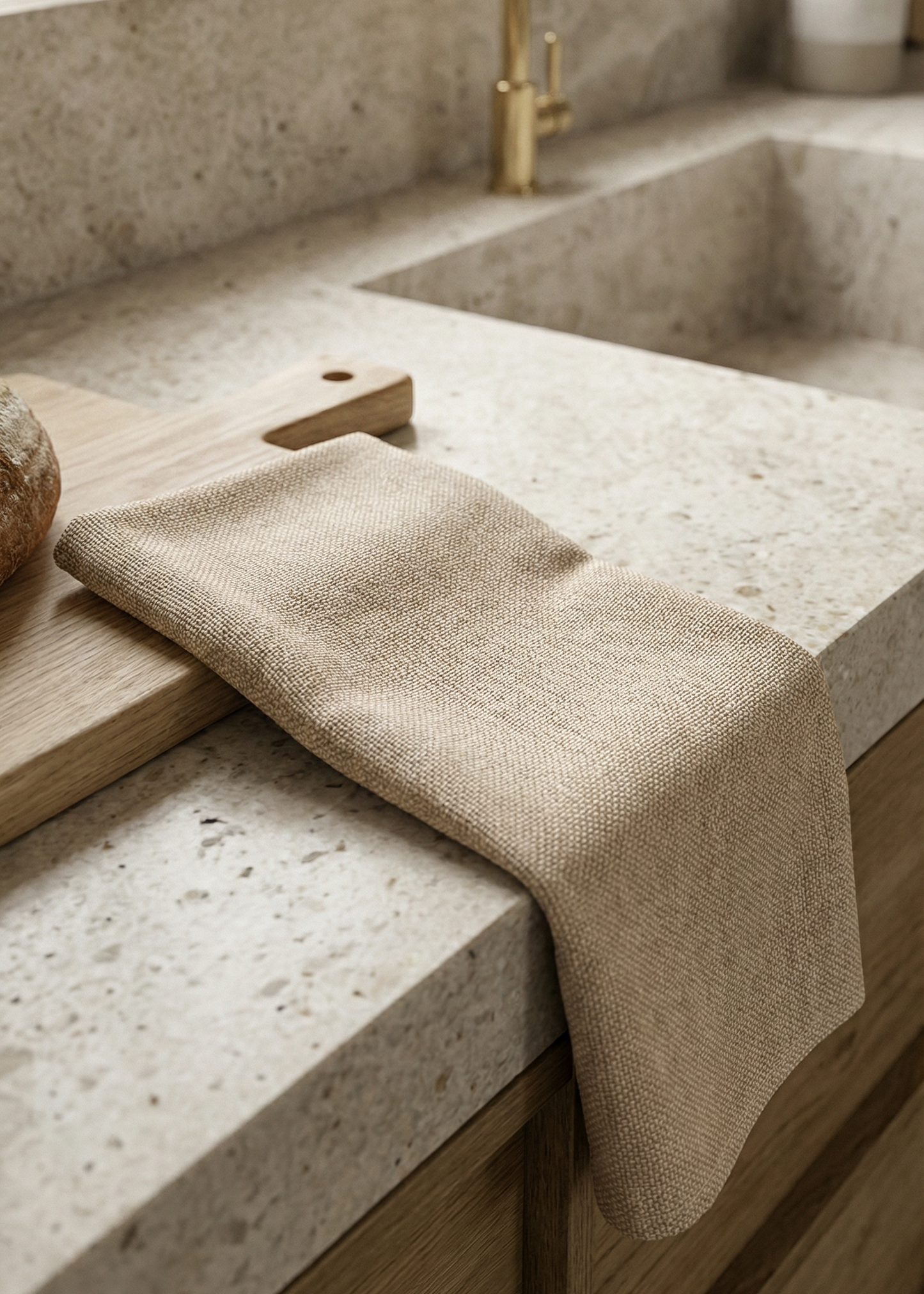 Beige kitchen towel draped over a countertop with a gold faucet in the background