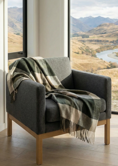 Gray armchair with a plaid blanket in a room with large windows showing a scenic view of mountains and a river.