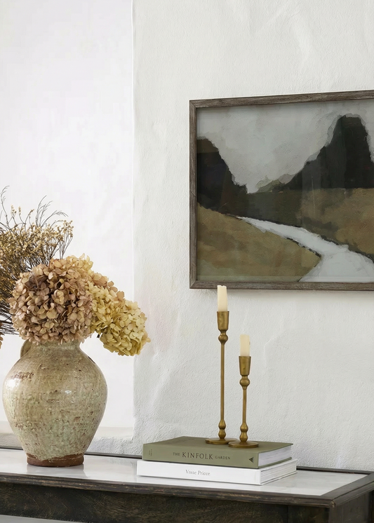 Decorative setup on a table with a vase, books, candles, and a framed landscape painting.