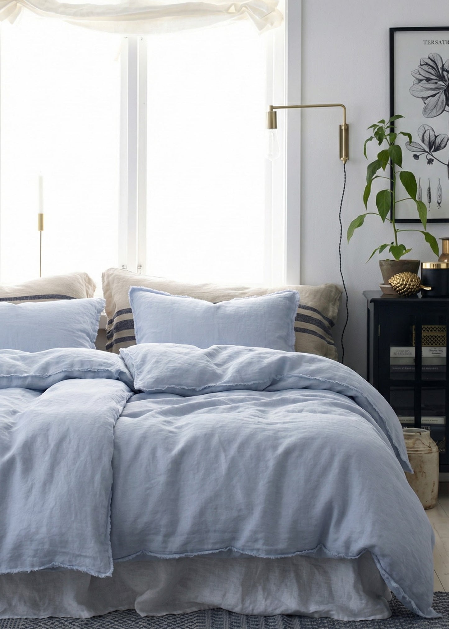 Cozy bedroom with light blue bedding and a window with white curtains.