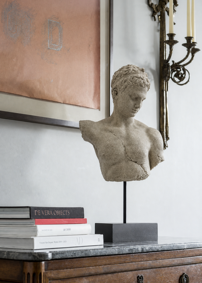 Decorative bust on a wooden dresser with books and a framed painting in the background.