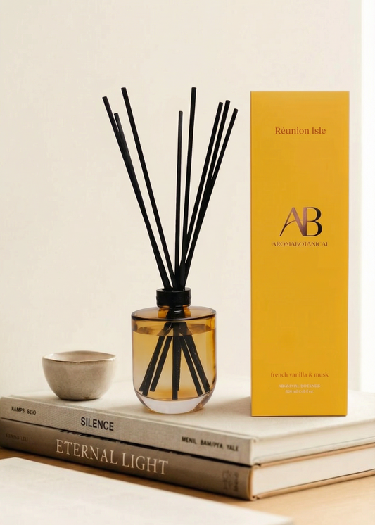 Aromatherapy diffuser with black sticks in a glass bottle next to a yellow box on books.