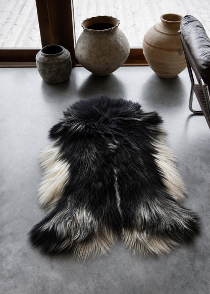 Black and white fur rug on a concrete floor with decorative vases in the background.