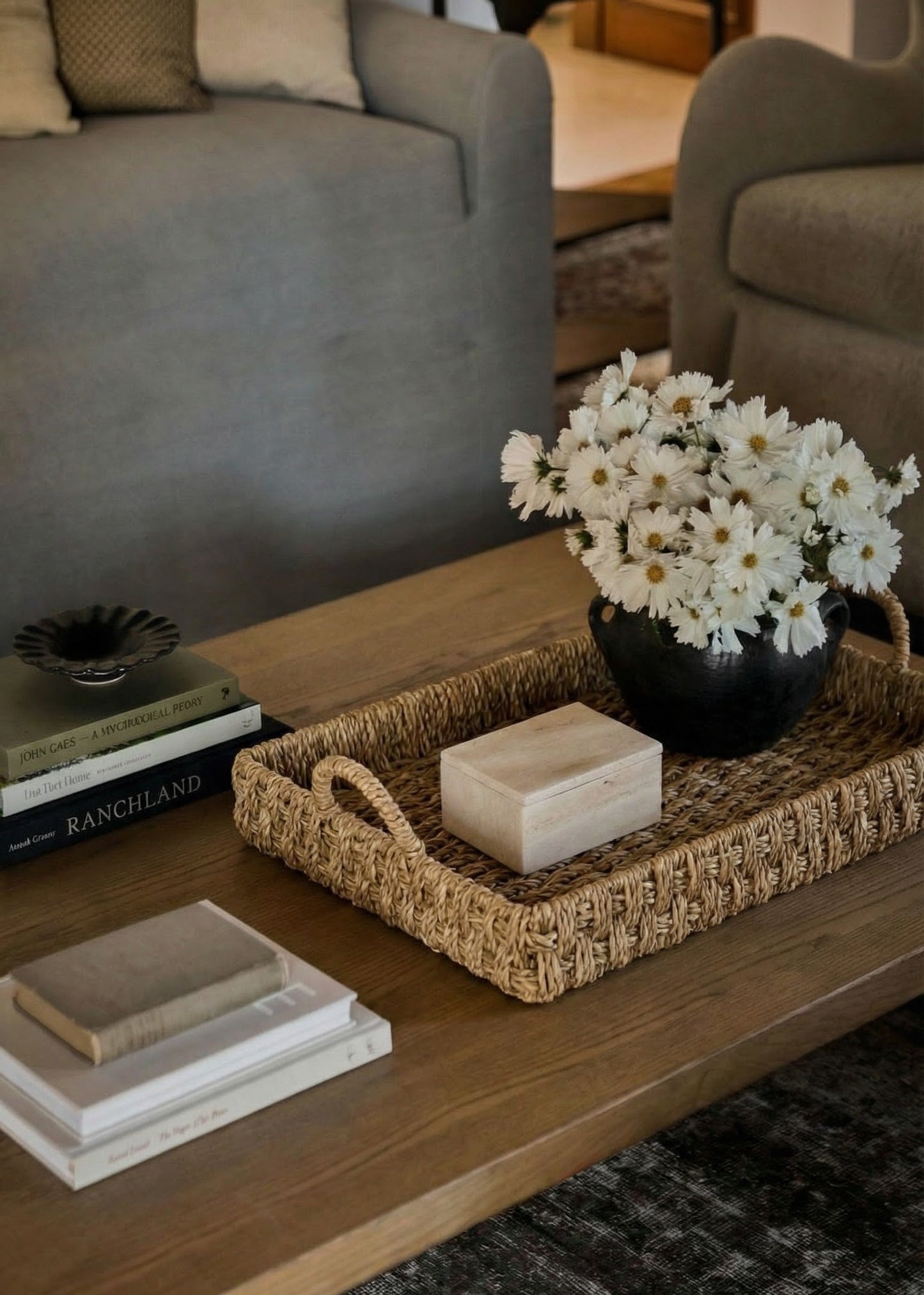 Living room with a coffee table featuring a vase of white flowers, books, and a woven tray.