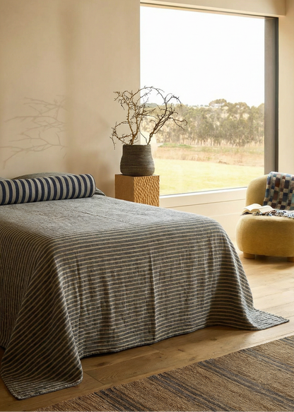 Cozy bedroom with a large window, striped bedding, and a vase with branches on a nightstand.