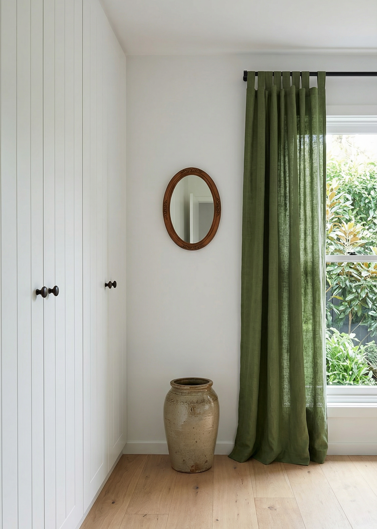 Room interior with green curtain, round mirror, and vase on a wooden floor.