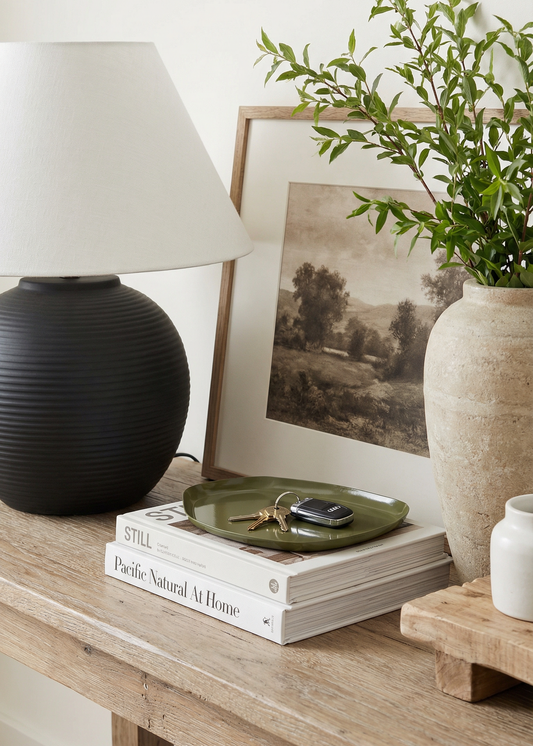 Decorative setup on a wooden surface with a black lamp, books, a plant, and a framed picture.