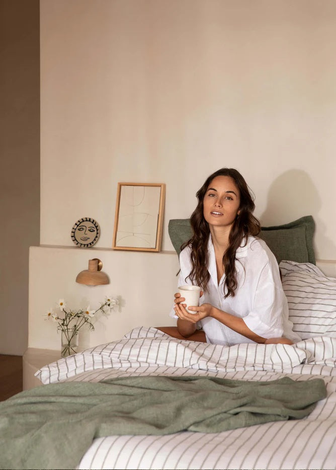 Woman sitting on a bed holding a mug in a cozy bedroom setting.