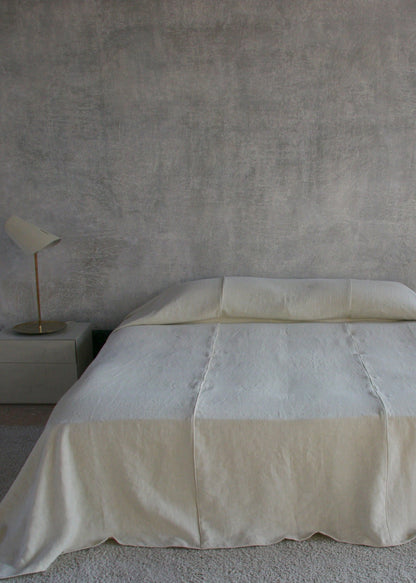 Beige bedspread on a bed in a minimalistic room with a gray wall and small plants.