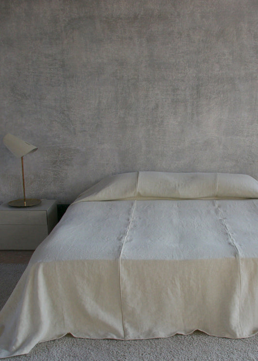 Beige bedspread on a bed in a minimalistic room with a gray wall and small plants.