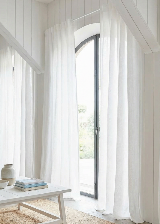 White curtains in a room with a wooden floor and a table.