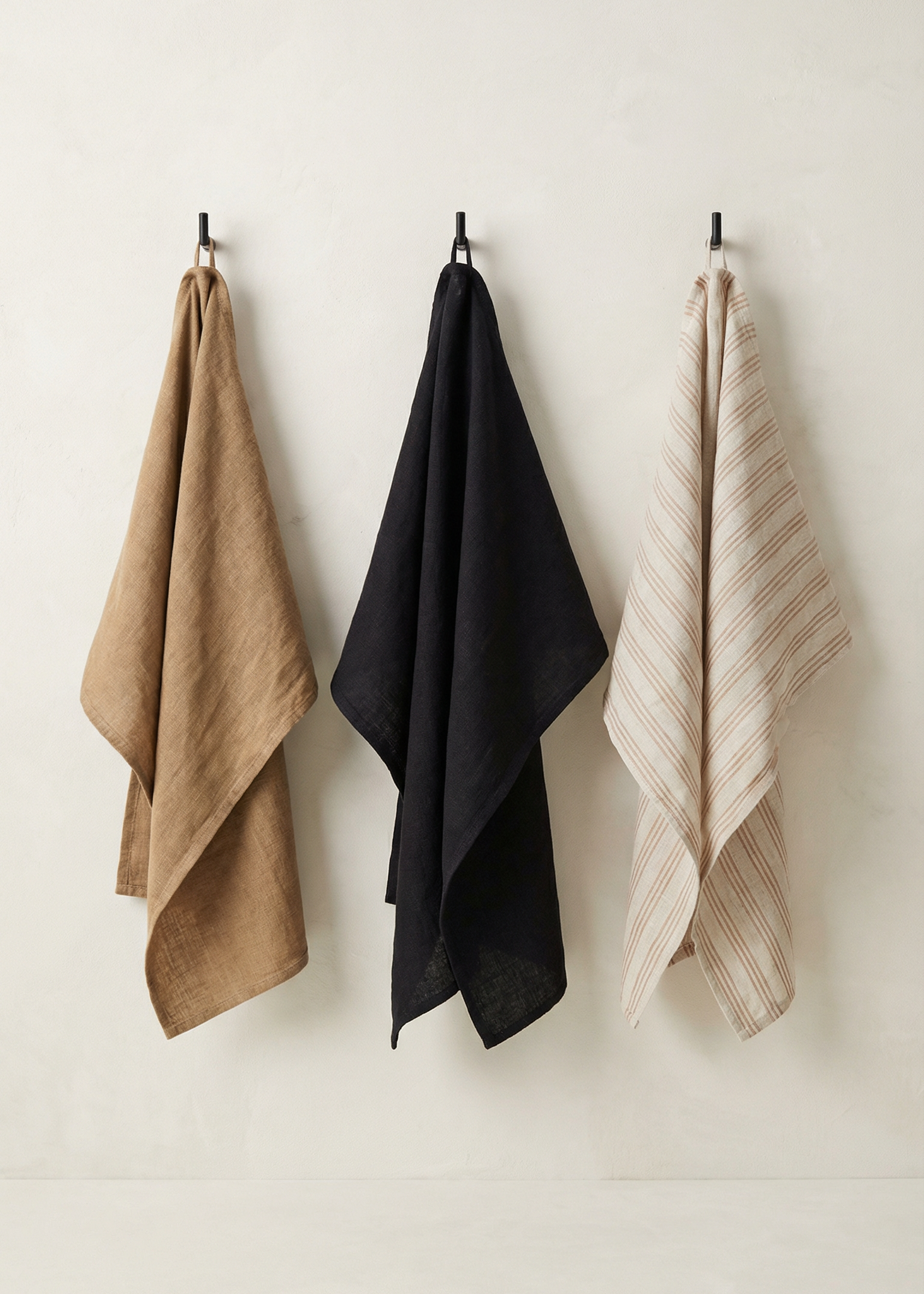 Three towels in brown, black, and beige hanging on a white wall.