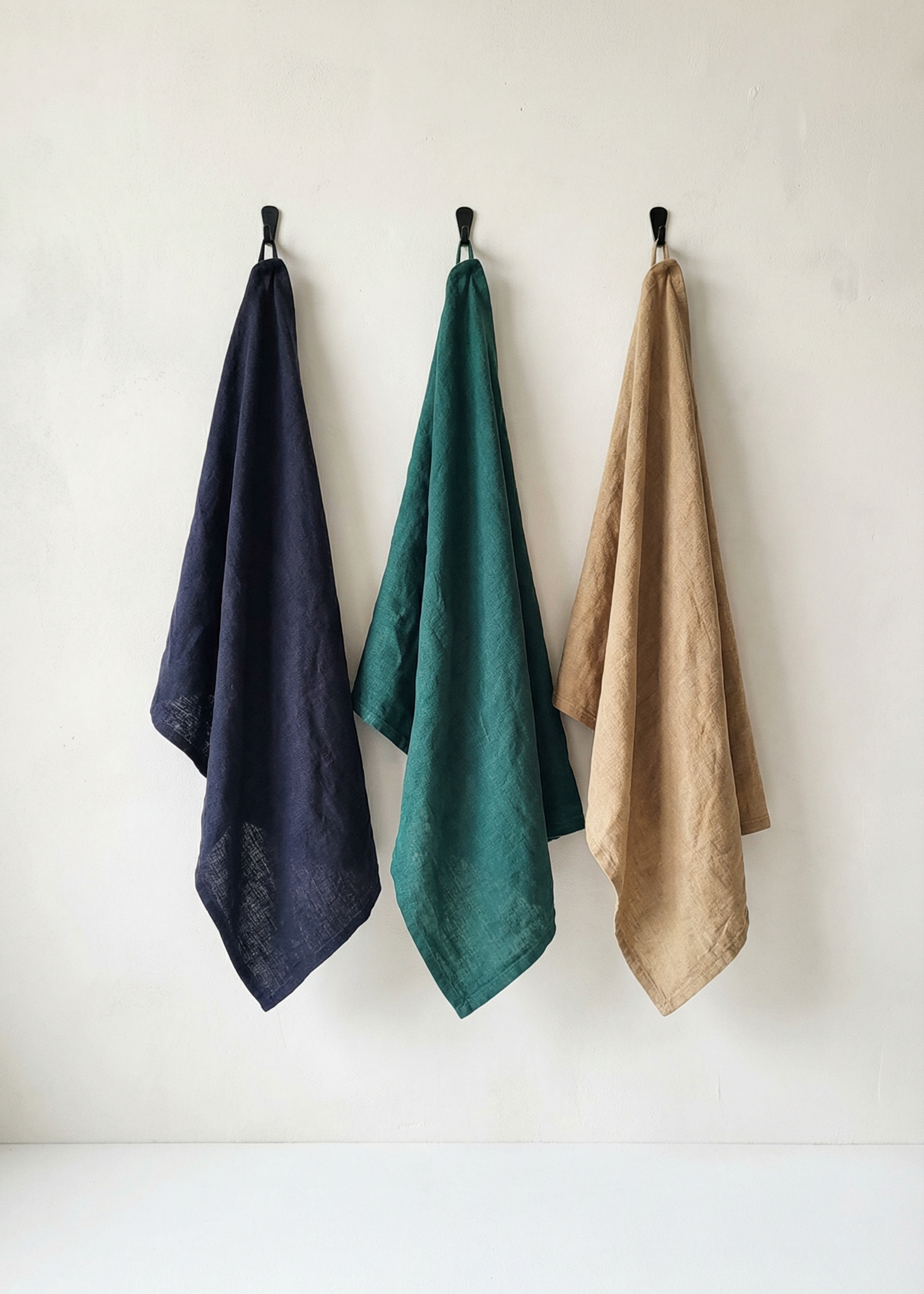 Three towels in navy, green, and beige hanging on a white wall.