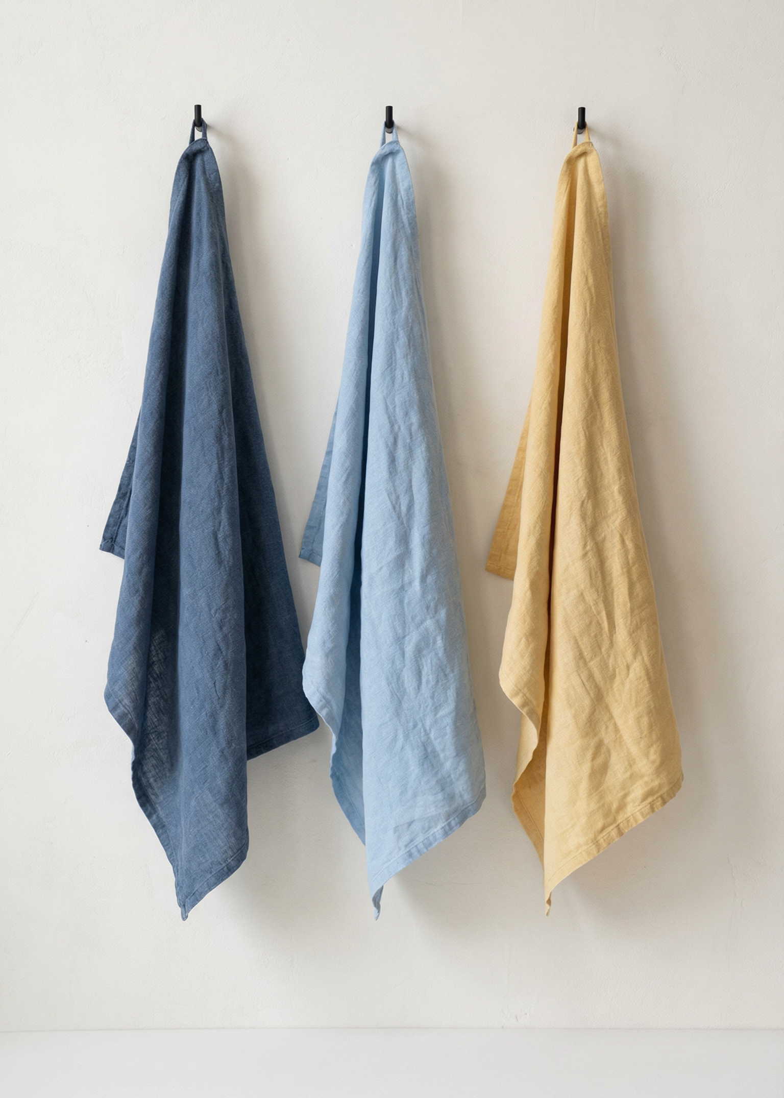 Three towels in blue, light blue, and yellow hanging on a white wall.