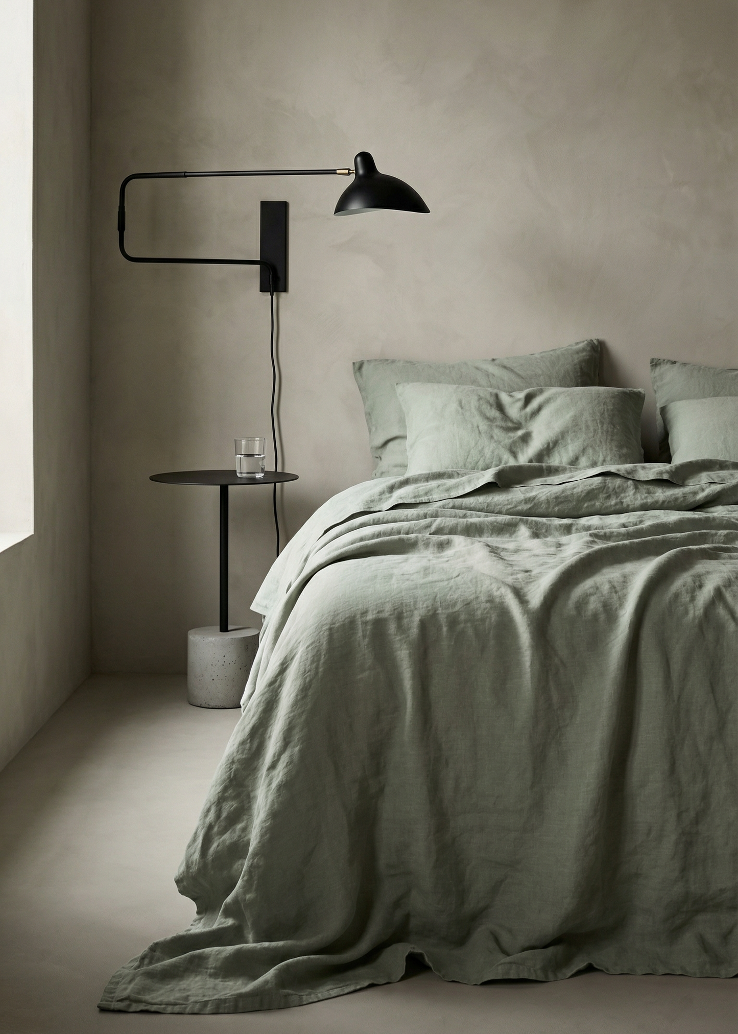Minimalist bedroom with a bed, lamp, and side table against a plain wall.