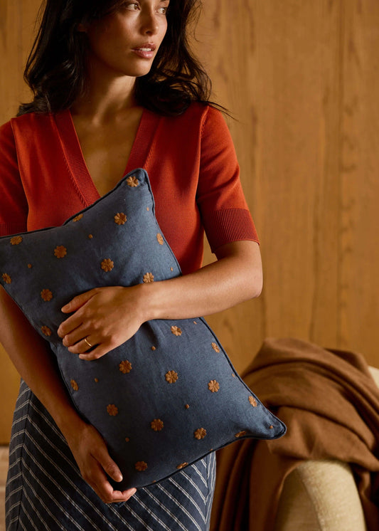 Woman holding a blue pillow with brown floral patterns against a warm-toned background