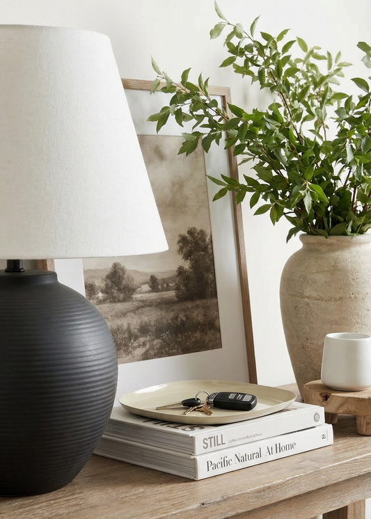 Decorative setup with a lamp, books, plant, and framed picture on a wooden surface.