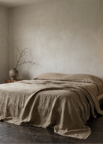 Bedroom with a bed covered in beige linens, a vase with branches, and a hanging light fixture.