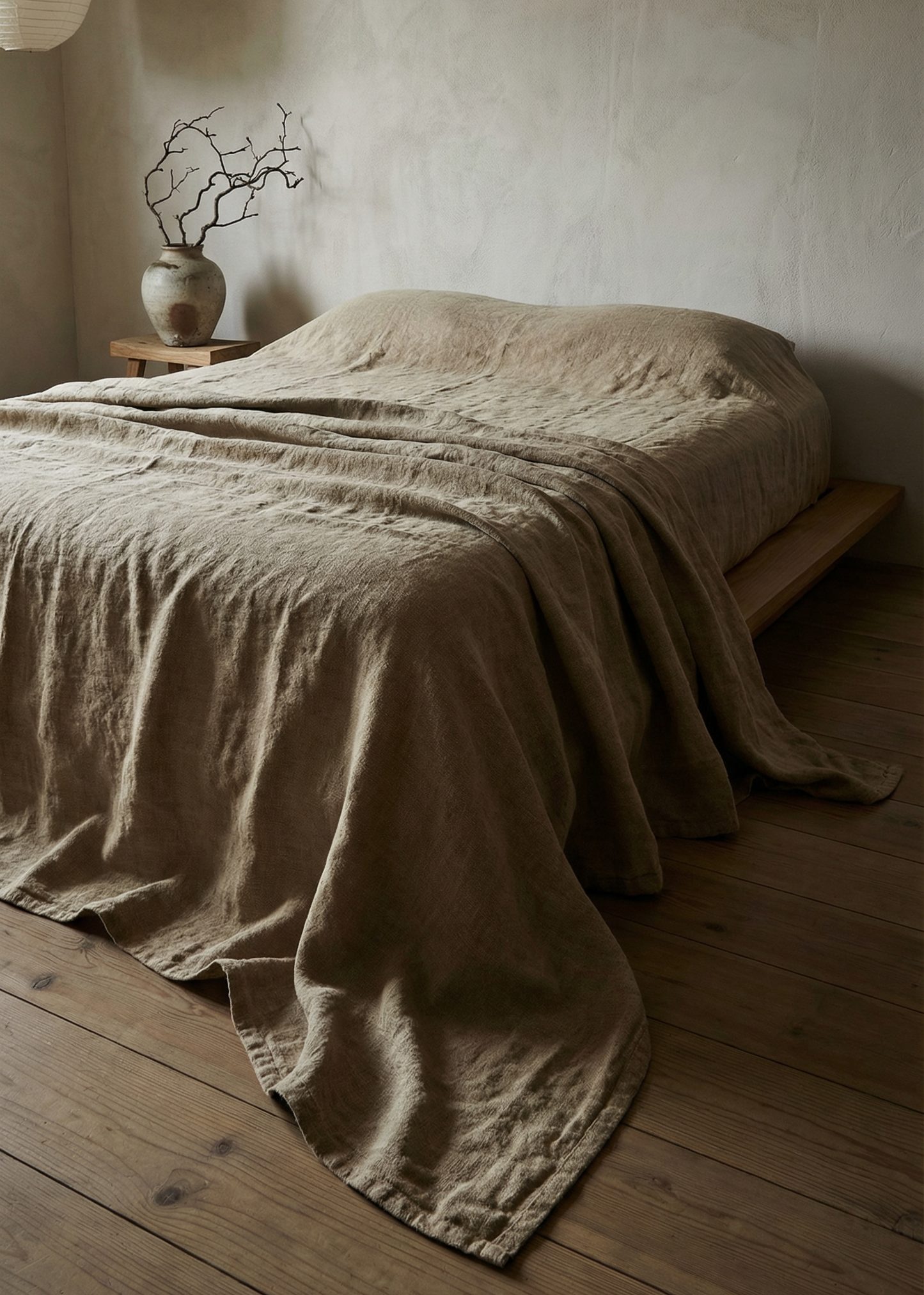 Beige textured blanket draped over a bed in a minimalistic room with wooden flooring.