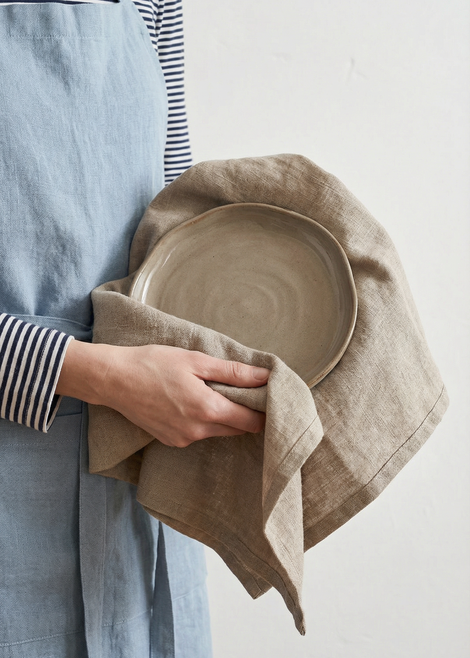 Person holding a ceramic plate wrapped in a cloth against a plain background