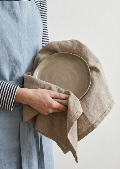 Person holding a ceramic plate wrapped in a cloth against a plain background