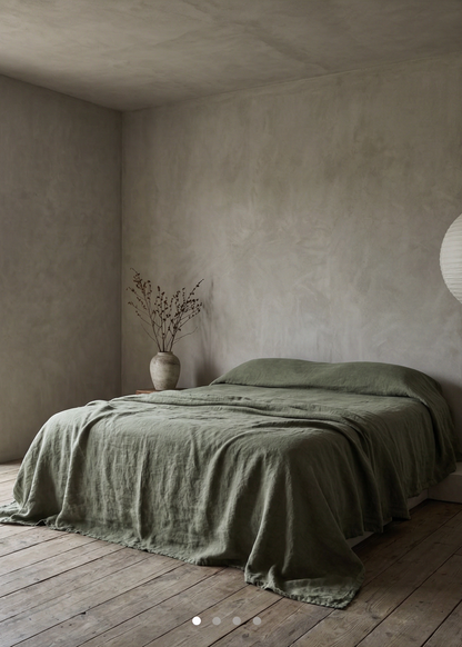 Bedroom with a bed covered in green bedding and a vase on a nightstand.