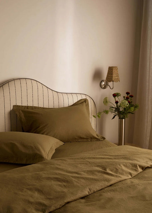 Bedroom with brown bedding, pillows, and a lamp on the wall.