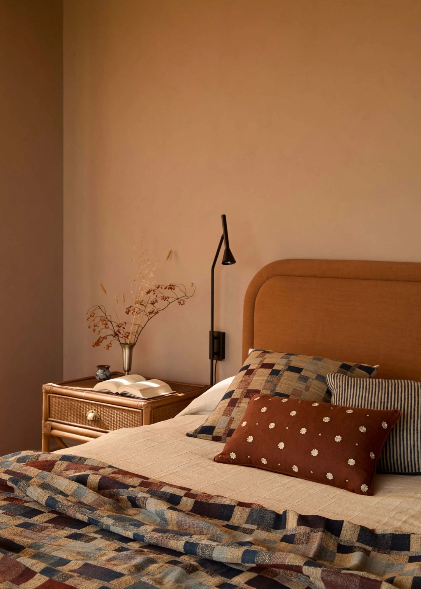 Bedroom with a bed featuring patterned bedding and pillows, a nightstand with a lamp, and a wall-mounted lamp.