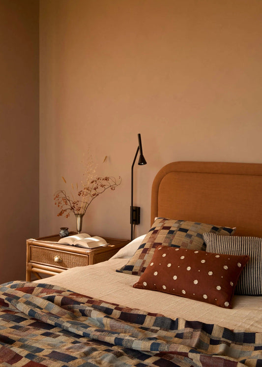 Bedroom with a bed featuring patterned bedding and pillows, a nightstand with a lamp, and a wall-mounted lamp.