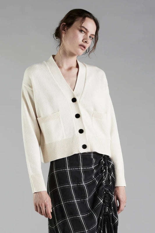 Woman wearing a cream cardigan with black buttons on a gray background