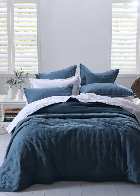 Blue bedding set on a bed with white pillows in a room with light gray walls and white blinds.