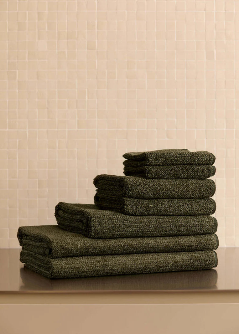 A set of olive green tweed towels neatly stacked on a bench.