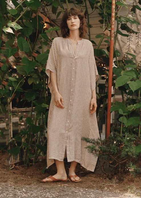 Woman wearing a long, light-colored striped dress standing in a garden setting.