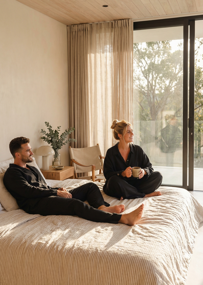 Two people sitting on a bed in a modern bedroom with large windows.