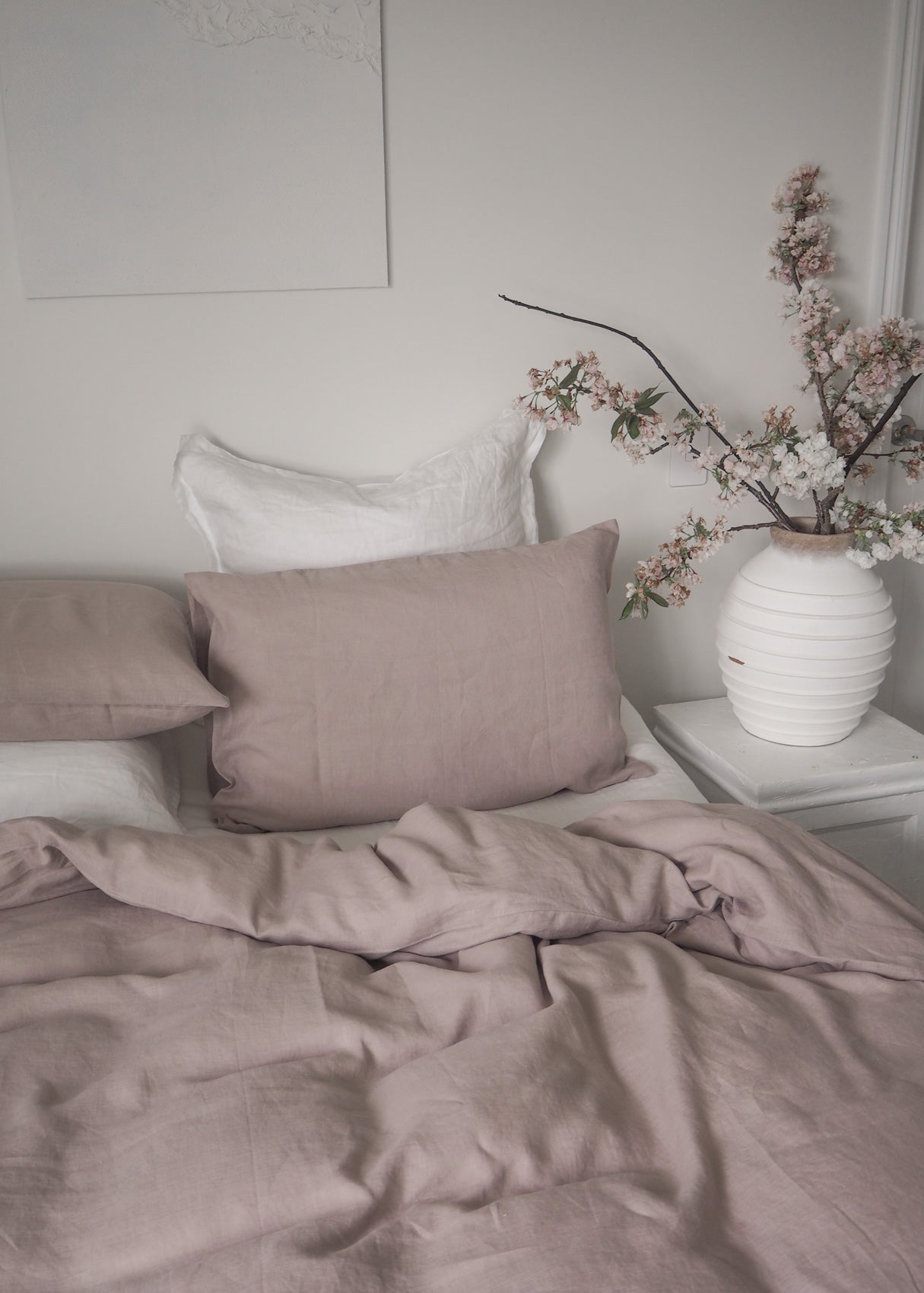 Neatly made bed with pink bedding and a vase of flowers on a nightstand.