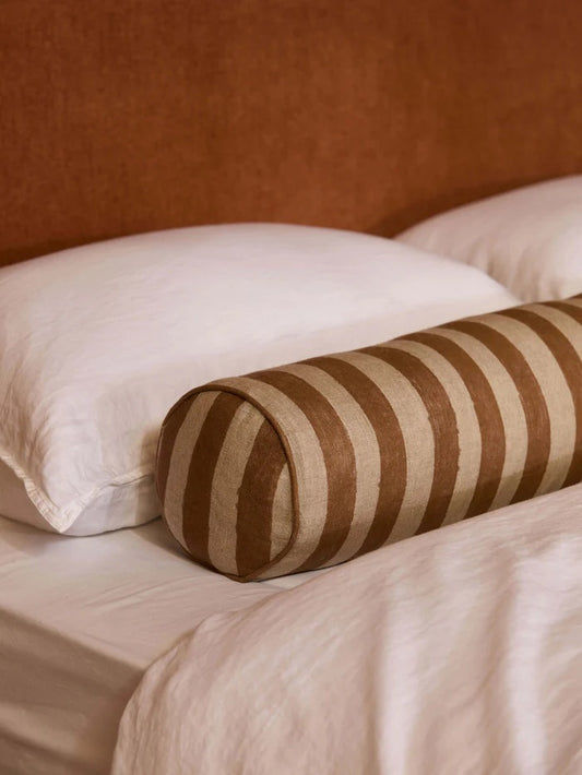 Striped cylindrical pillow on a bed with white pillows and beige bedding.