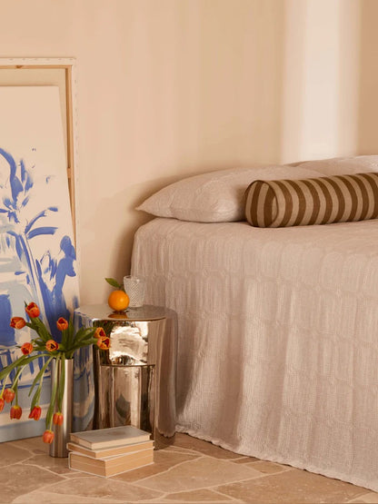 Neatly made bed with striped pillow, side table with flowers and books, and abstract art on wall.