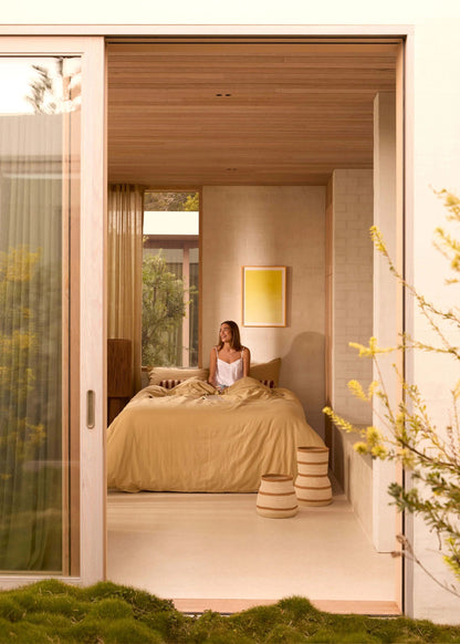 Woman sitting on a bed in a modern bedroom with a view of greenery outside.