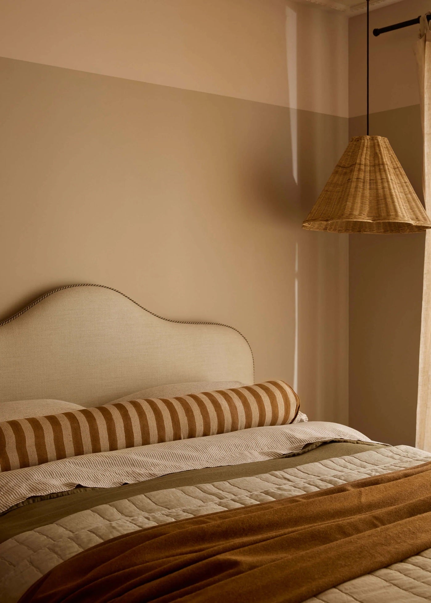 Bedroom with a bed featuring striped pillows and a wooden headboard, illuminated by a hanging lamp.