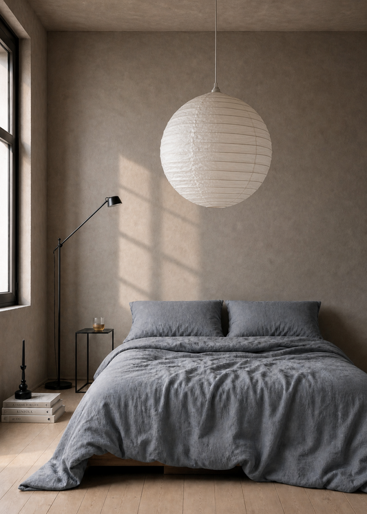 Modern bedroom with gray bedding, a white pendant lamp, and minimal decor.