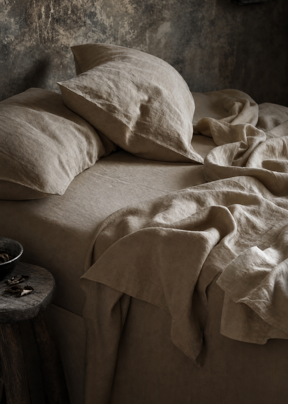 Bed with beige pillows and sheets against a textured wall.