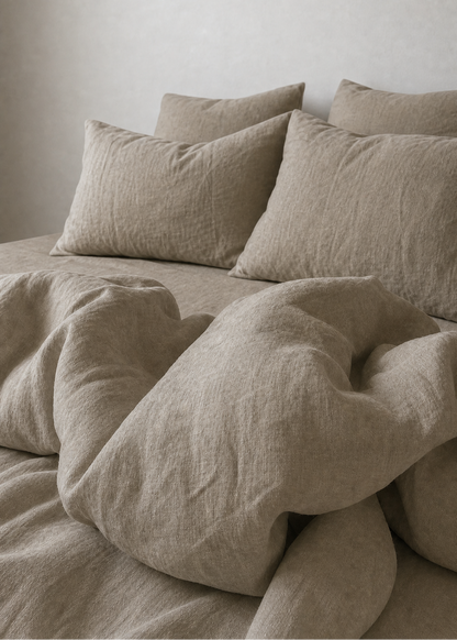 Beige bedding with pillows on a bed against a plain wall