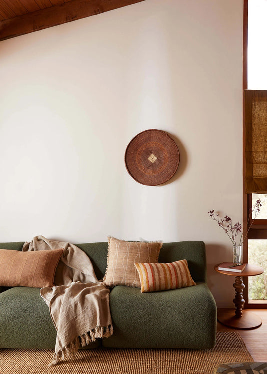 Cozy living room with a green sofa, decorative pillows, and a wooden wall hanging.