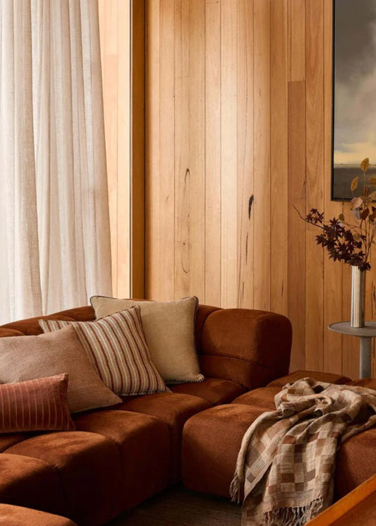 Cozy living room with brown sectional sofa, wooden walls, and a painting.