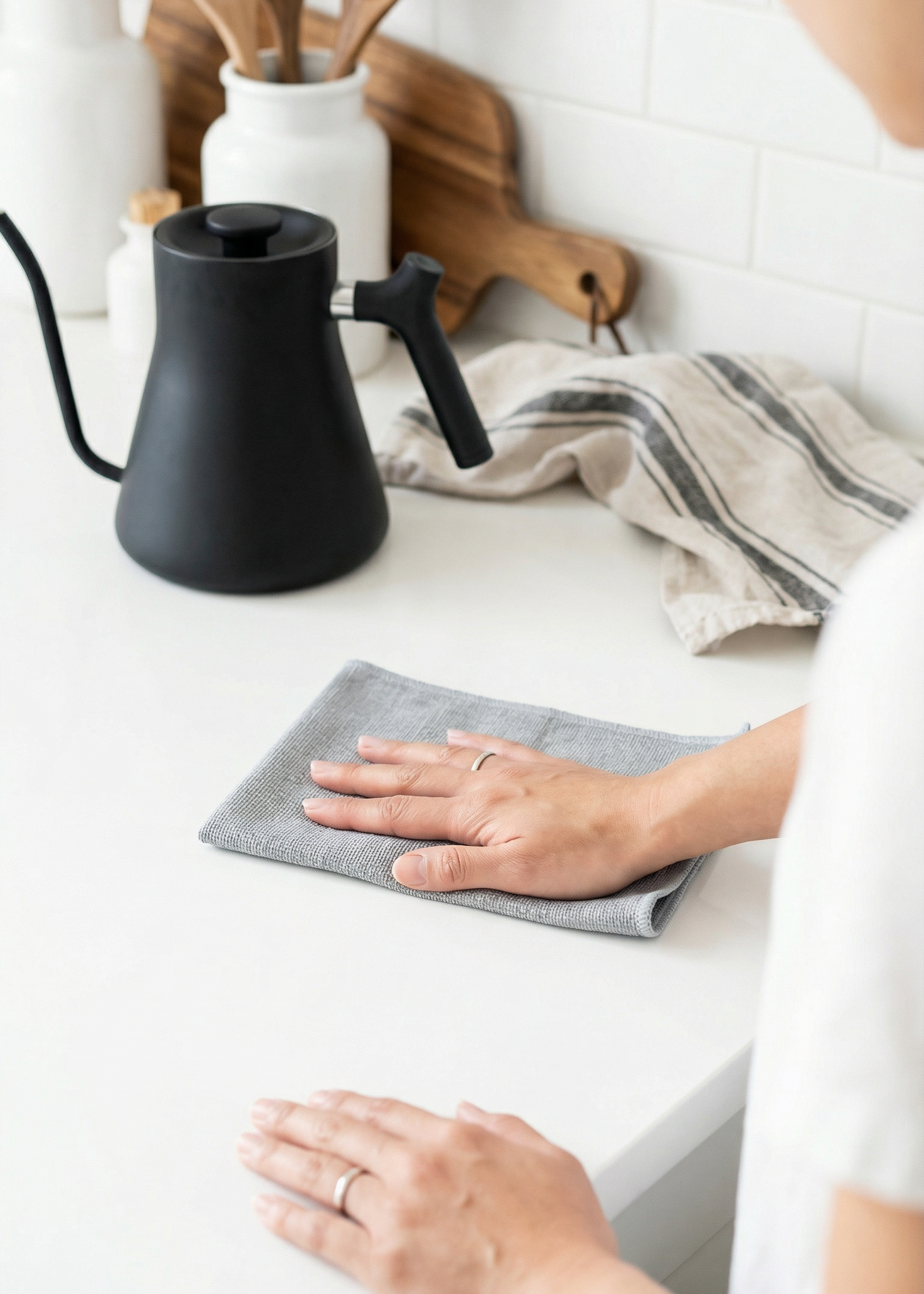 Person cleaning a kitchen counter with a cloth, next to a black coffee maker.