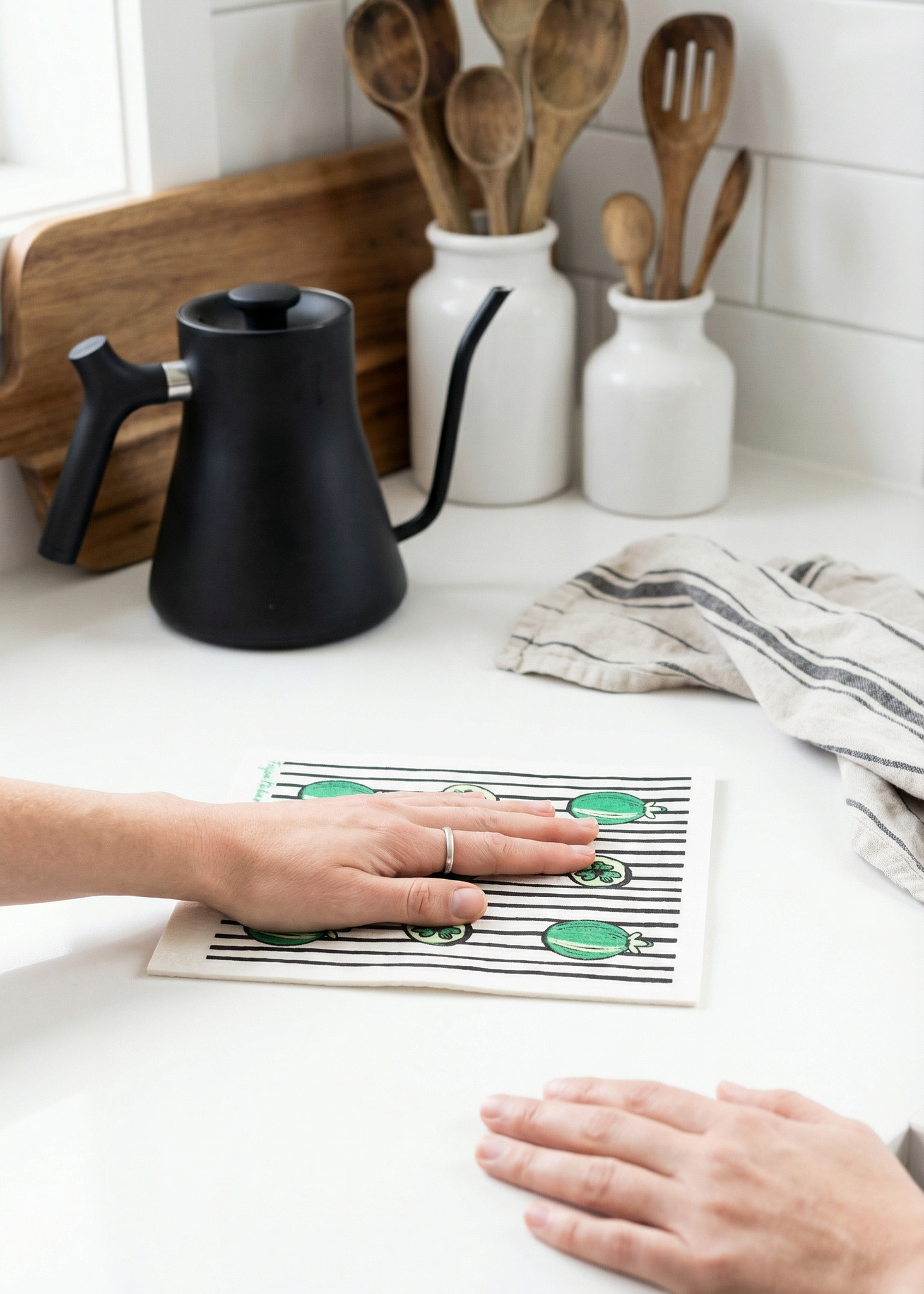 Person using a kitchen mat with green designs on a white countertop.