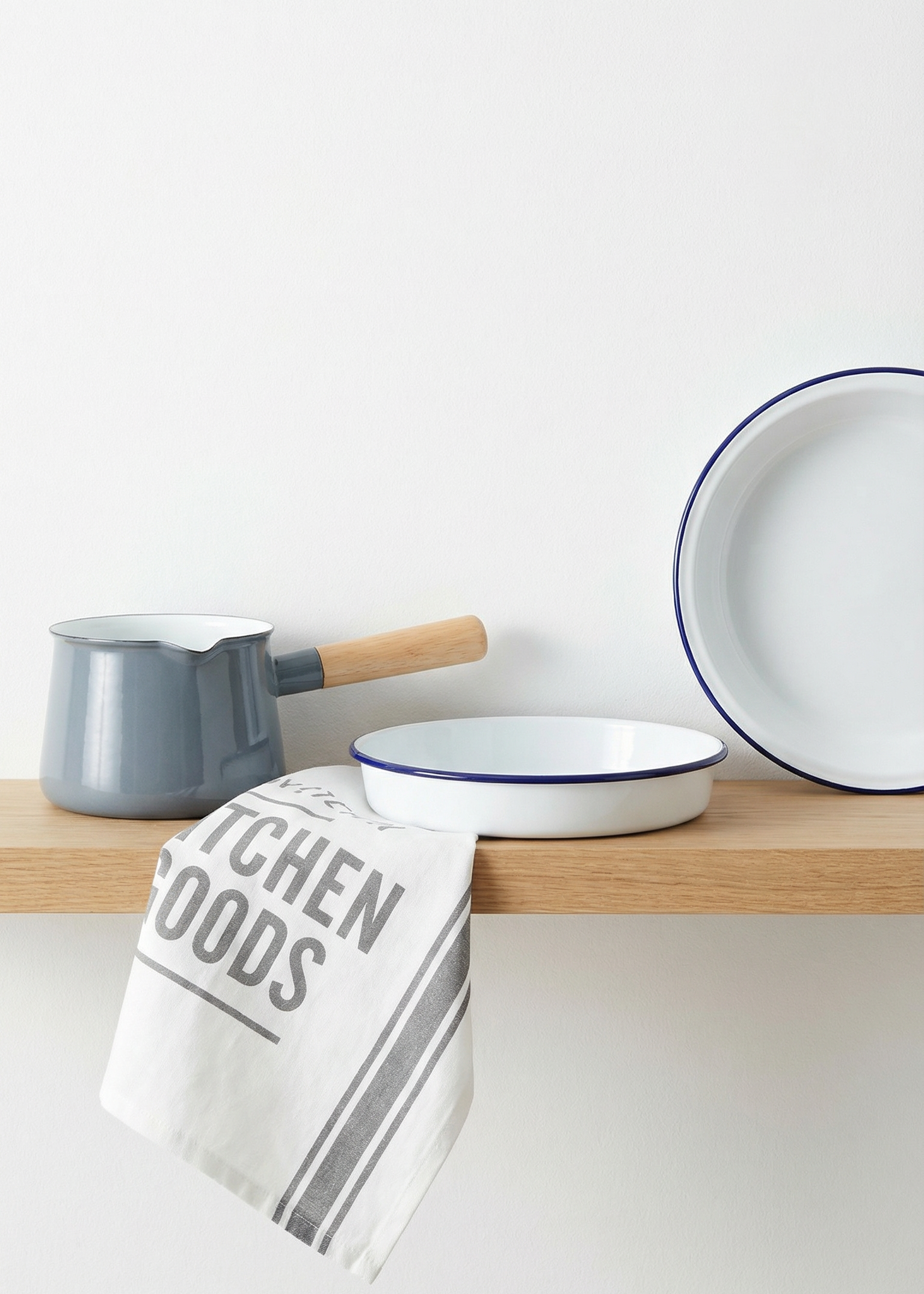 Enamelware including bowls and a ladle on a wooden shelf with a kitchen towel.