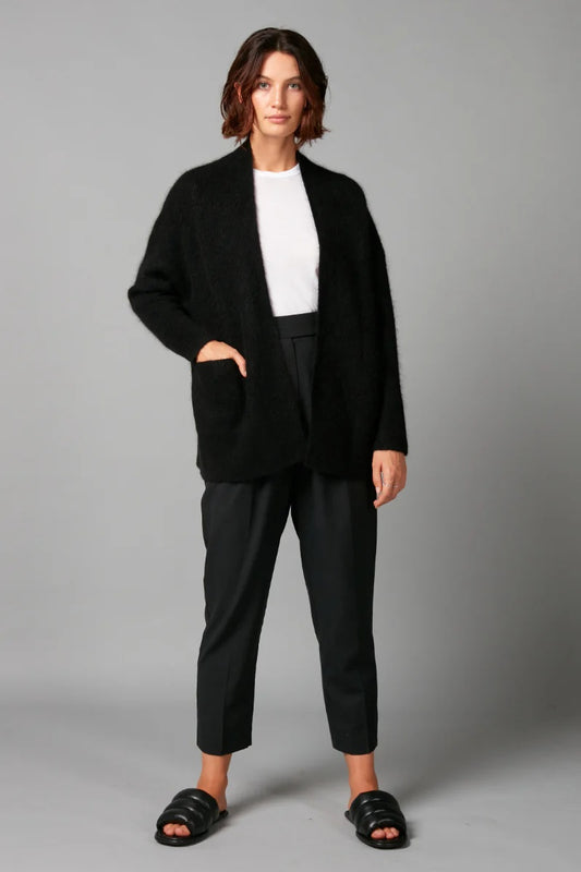 Person wearing a black coat, white shirt, and black pants on a gray background