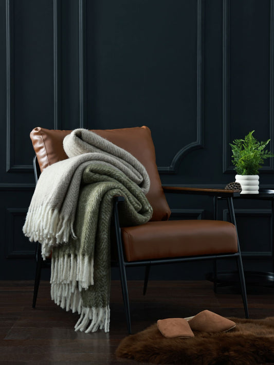 Brown leather chair with a green and white blanket draped over it against a dark paneled wall.